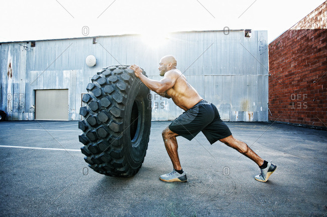 Black man working out with heavy tire outdoors stock photo - OFFSET