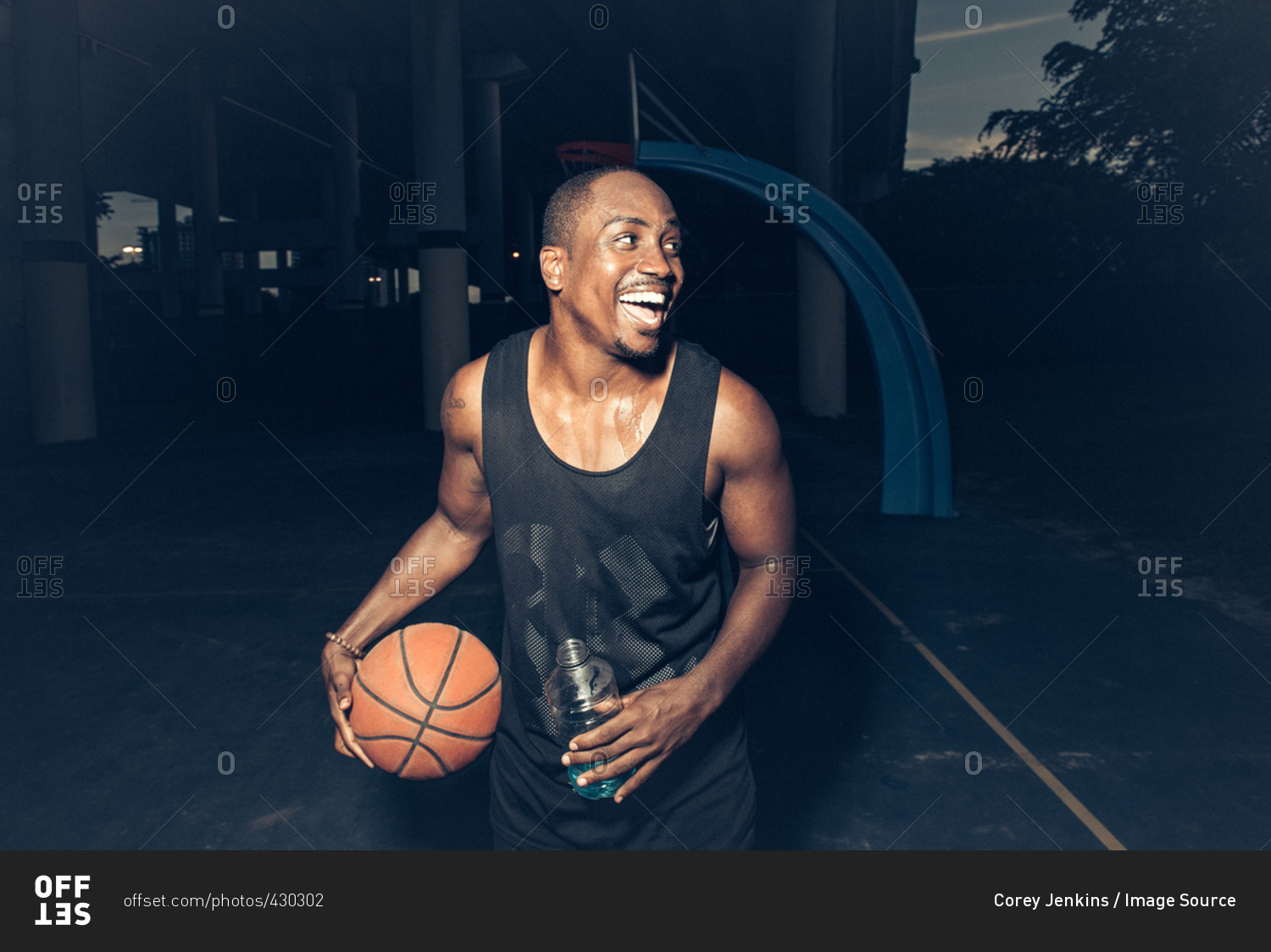 Man on basketball court holding basketball looking away smiling
