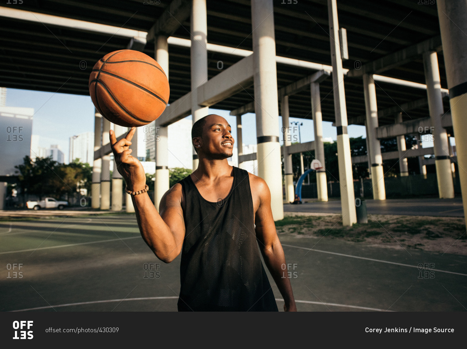 Man on basketball court balancing basketball on finger looking away