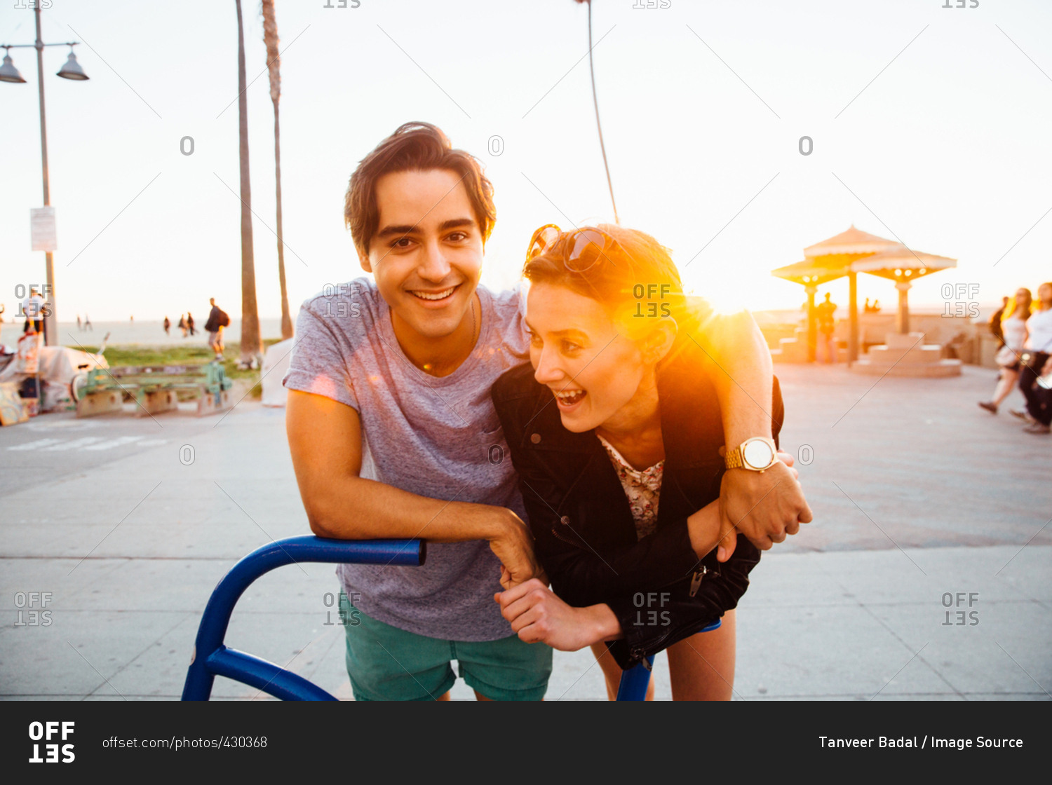 Portrait of happy young couple leaning against bicycle sculpture at coast, Venice Beach, California, USA