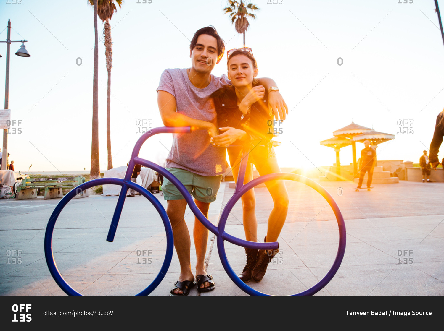 Portrait of young couple leaning against bicycle sculpture at coast, Venice Beach, California, USA