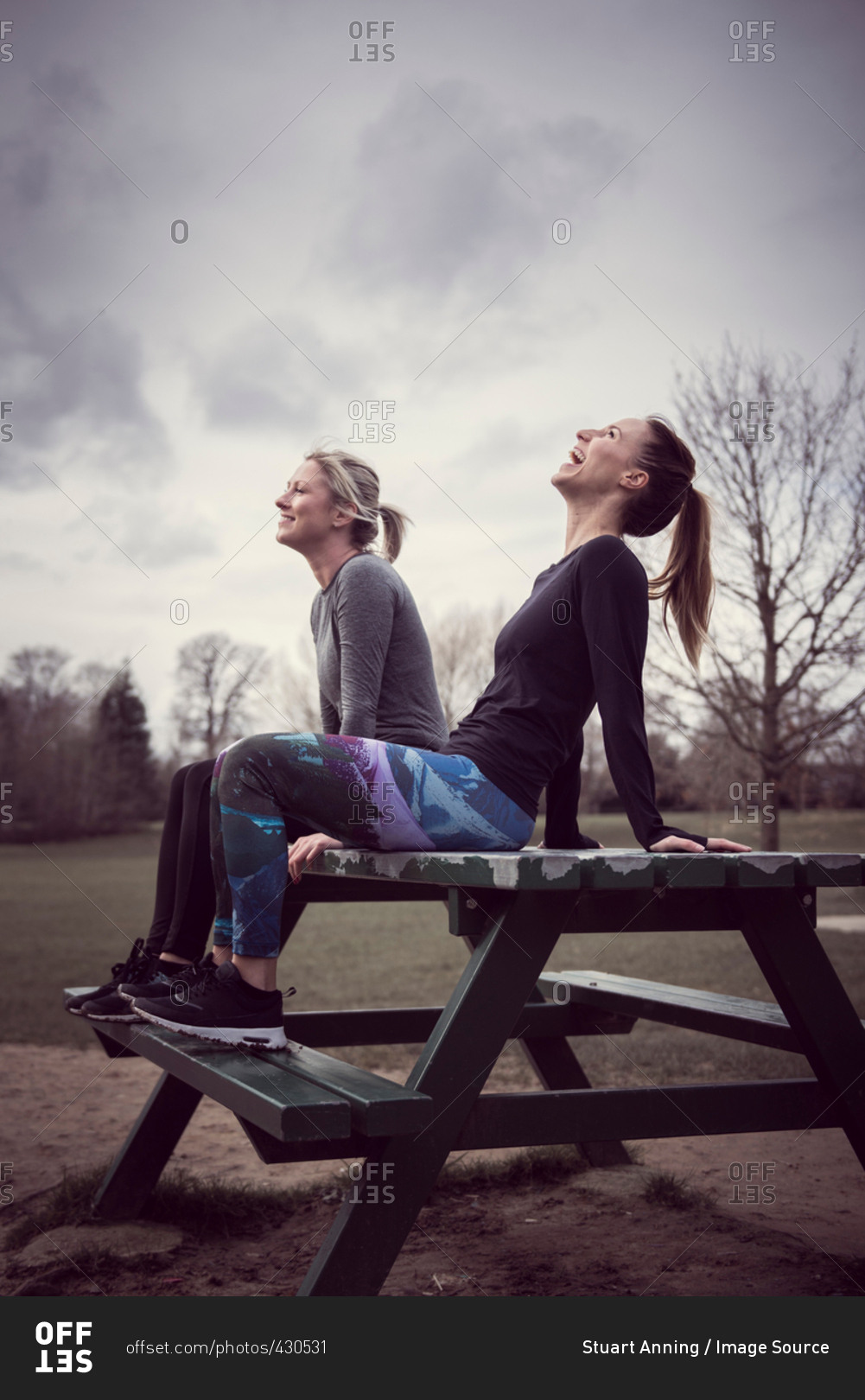 Women wearing sports clothing sitting on picnic table, head back laughing