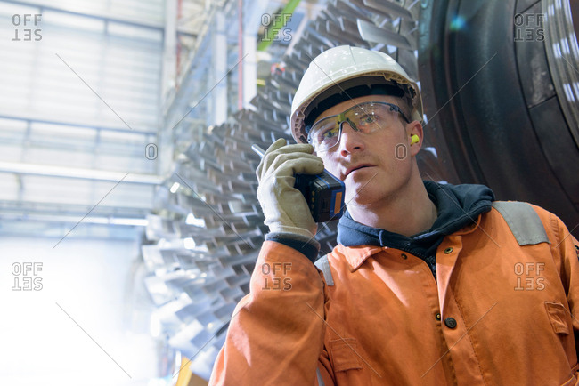 Worker with walkie talkie in front of gas turbine in gas-fired power station