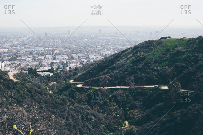 Elevated view of hills and winding road with distant smoggy cityscape, Los Angeles, California, USA