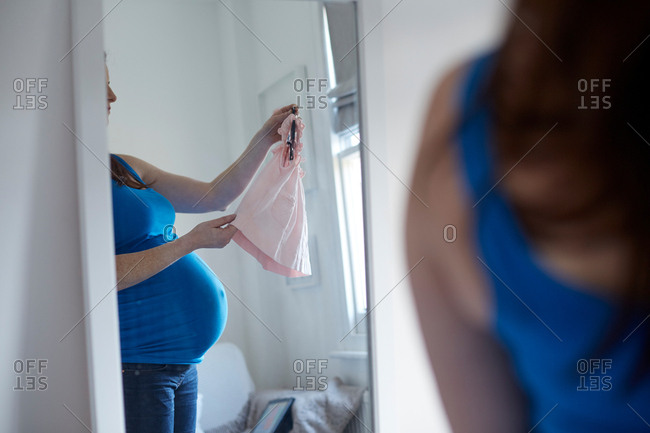 Mirror image of pregnant mother holding baby clothes on clothes hanger
