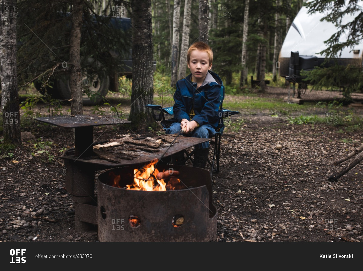 Boy sitting beside a campfire roasting a hot dog