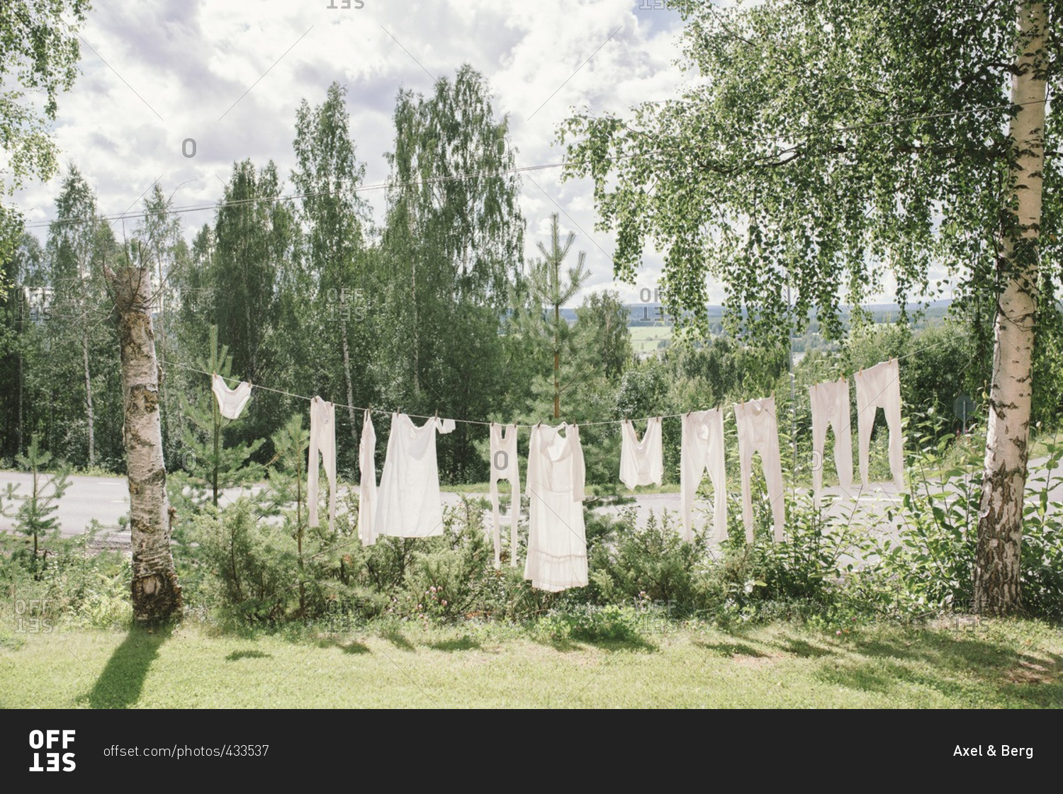 White linens hanging on a clothesline between two trees stock photo