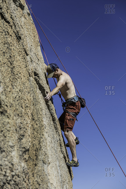 Sierra Nevada, California - July 16, 2016: Rock climber clings to ridge in rock face while ascending cliff