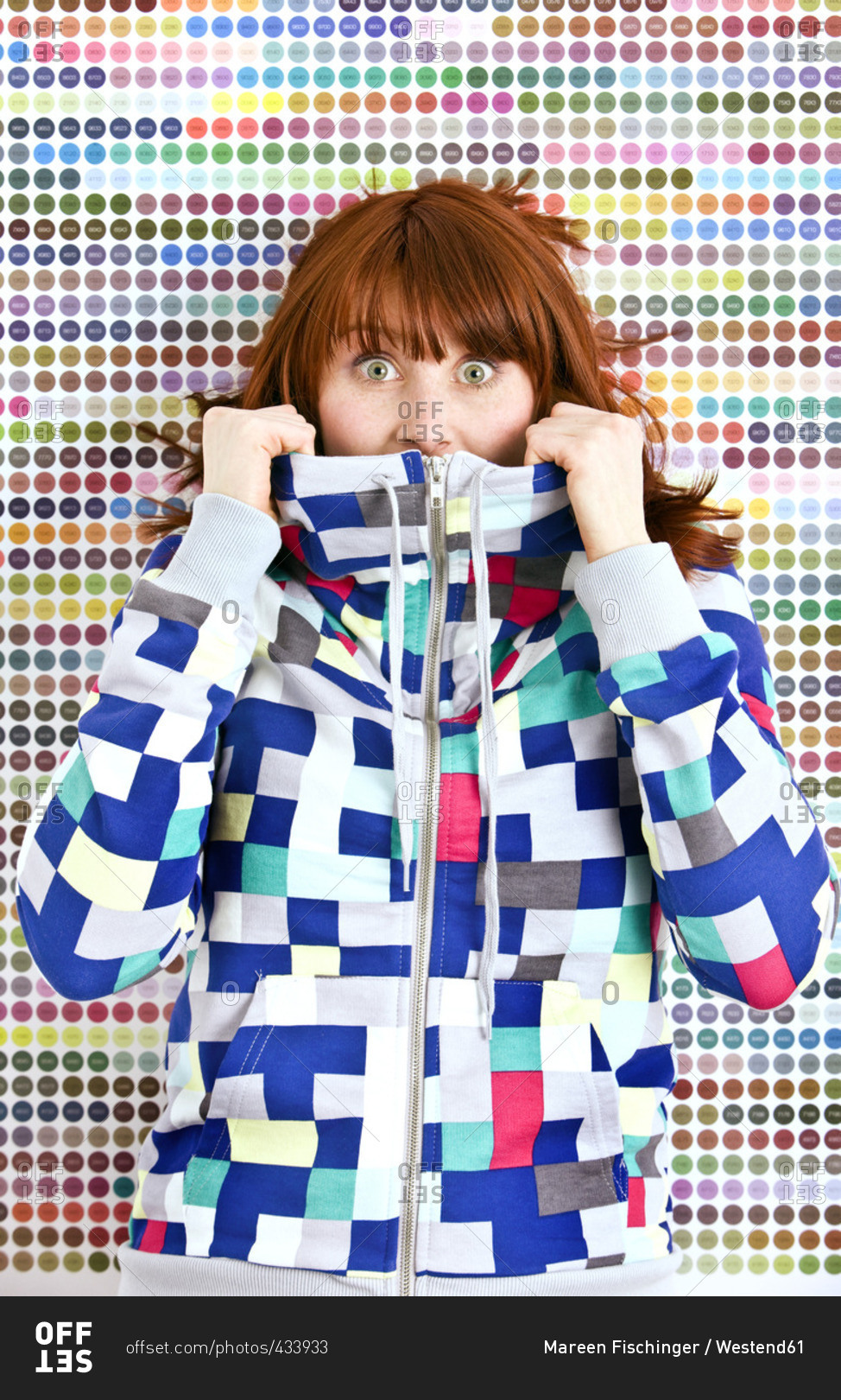 Frightened young woman wearing patterned jacket in front of dotted wall