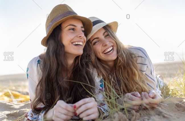 Portrait of two best friends with summer hats lying on the beach
