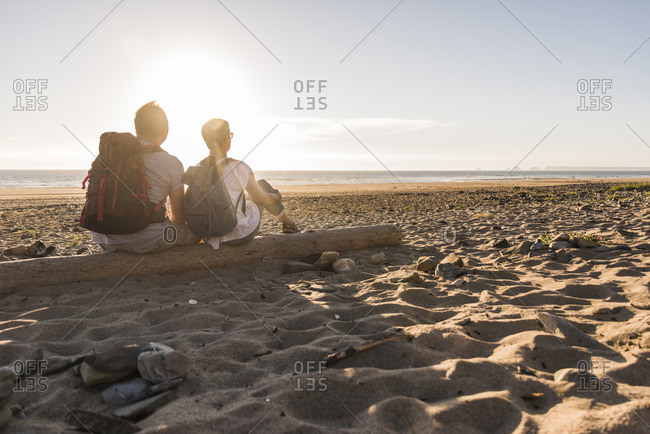 France, Bretagne, Finistere, Crozon peninsula, couple during beach walk, sitting on beach, enjoying sunset