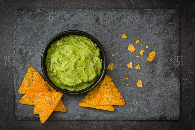 Tasty guacamole and chips on a black stone cutting board