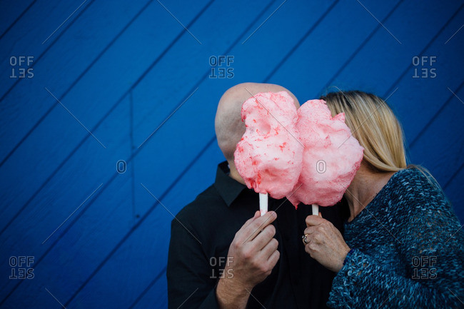 Man and a woman hiding behind pink cotton candy kissing in front of a blue wall