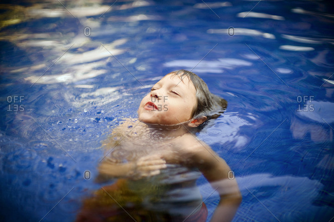 Young boy blowing bubbles in a swimming pool.