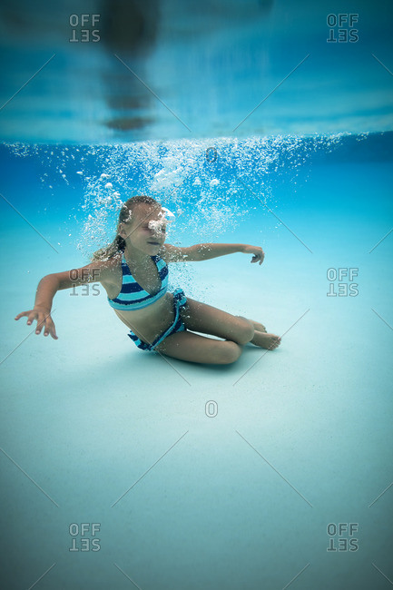 Young girl swimming underwater in a pool.
