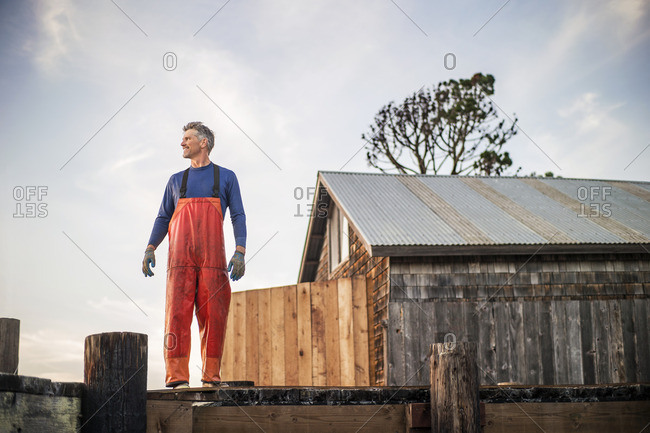 Fisherman in waders standing on a wooden pier.