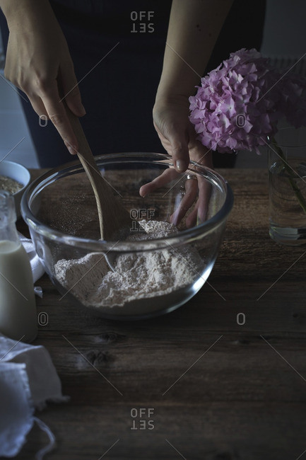 Hands mixing flour with a wooden spoon in a bowl on a rustic wooden table