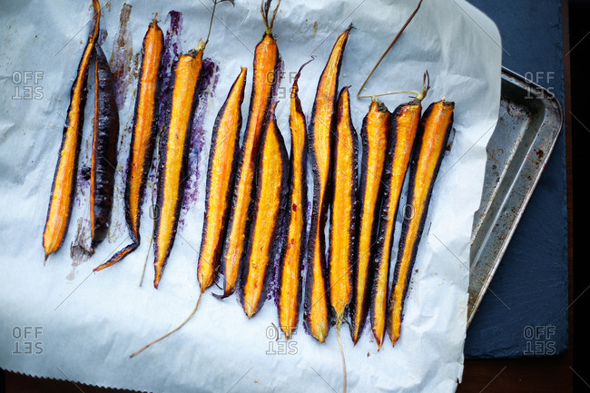 Roasted sliced purple carrots lined on parchment paper and seasoned with oil and salt