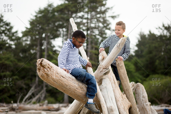 Two brothers playing on a driftwood shelter on a beach