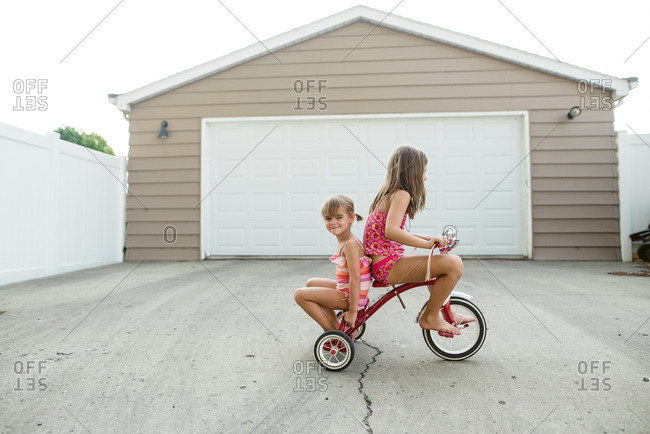 Two sisters in bathing suits sitting on a tricycle