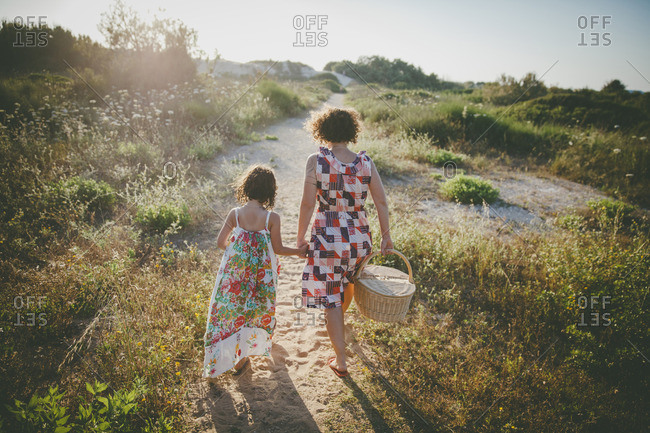 Mother and daughter holding hands walking to the beach with a picnic basket