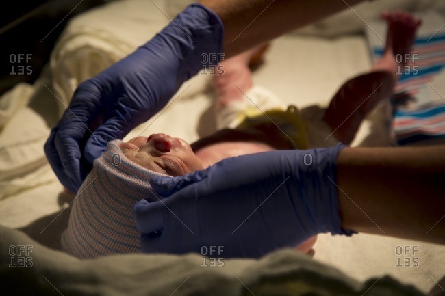A hat is put on a newborn baby as a nurse wears purple latex gloves