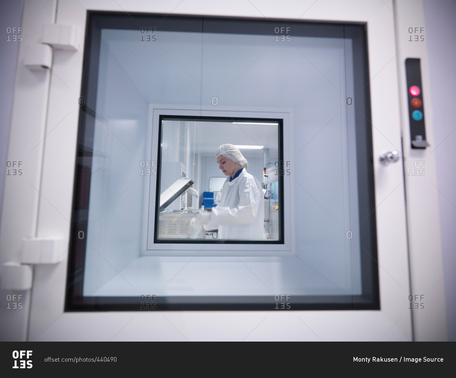 View through clean room hatch, of female scientist working with product in an engineering factory clean room