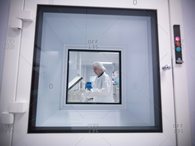 View through clean room hatch, of female scientist working with product in an engineering factory clean room