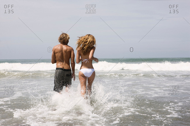 Back view of little girl in panties carrying blue swimming board while  walking on wet sand near sea stock photo - OFFSET