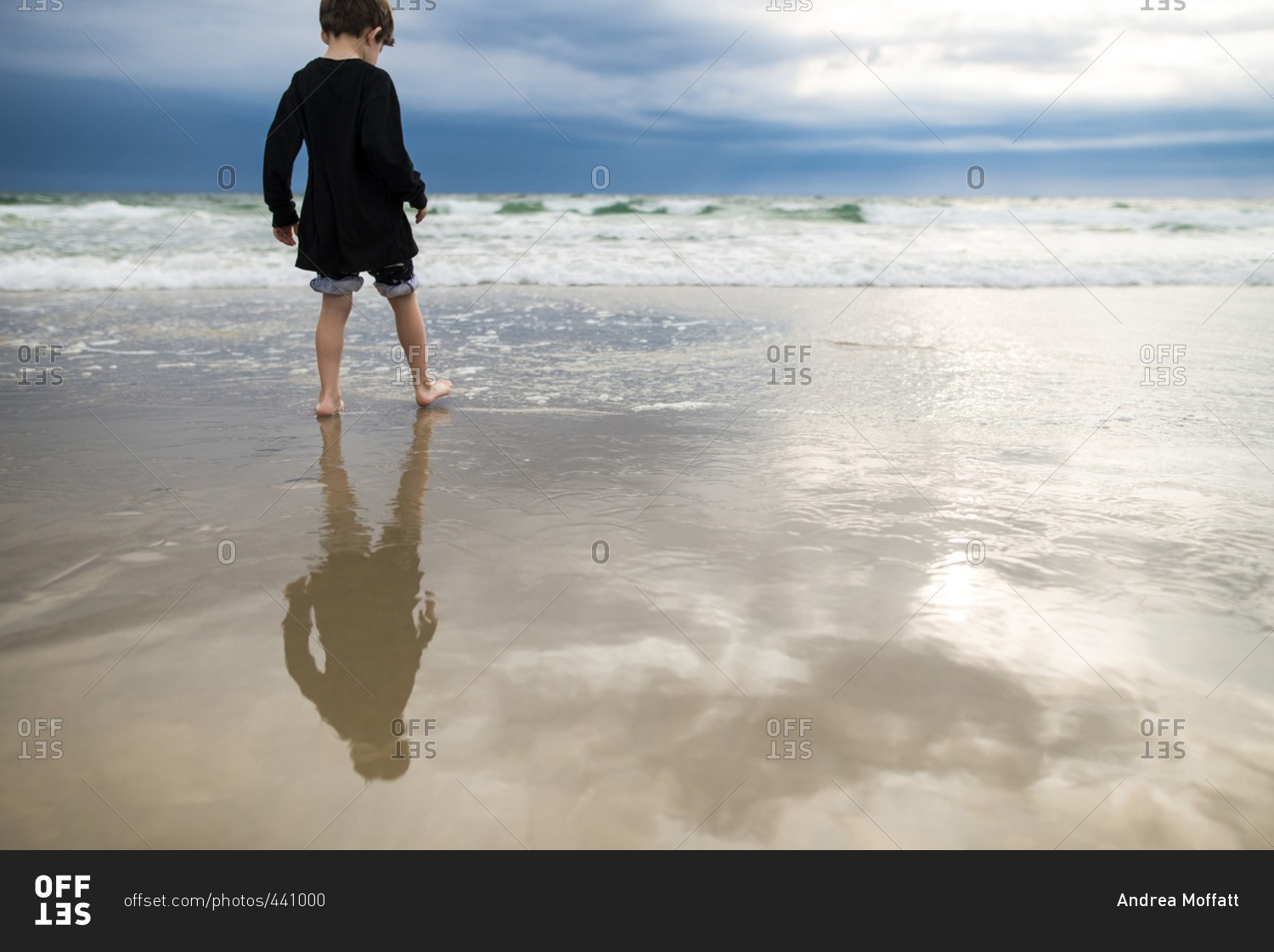 Reflection of young boy on wet sand on beach stock photo - OFFSET