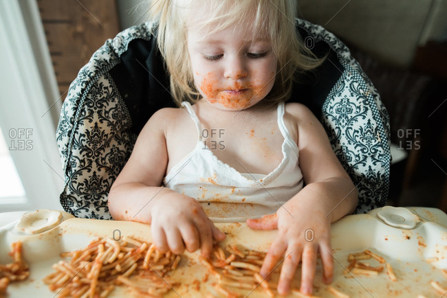 Girl sitting in a high chair eating a messy meal of spaghetti