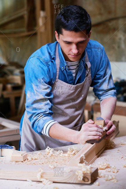 Craftsman using a shaving wood with a wood plane in his workshop