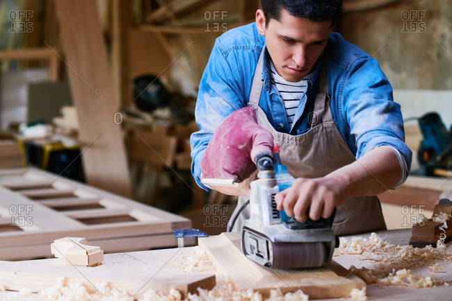 Craftsman using a belt sander to smooth wood in his workshop