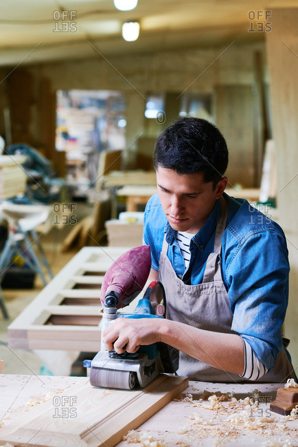 Man using a belt sander to smooth a piece of wood in his workshop