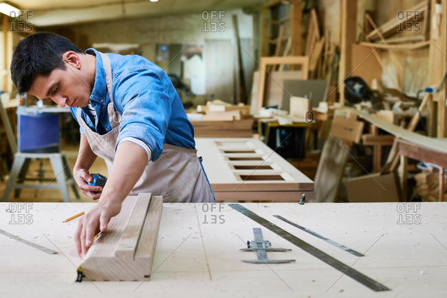 Man using a tape measure to measure the length of a board in his workshop