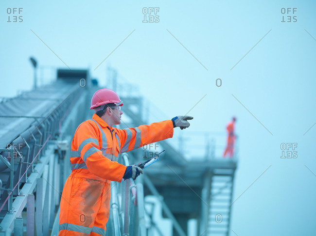 Workman in reflective clothing pointing from steps of screening conveyor at quarry