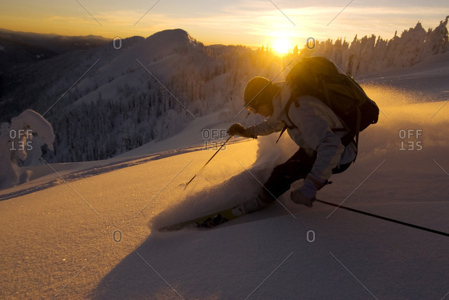 Woman ski instructor backlit with alpenglow, sunset, skiing powder down Evening Ridge, Whitewater ski resort, Nelson, British Columbia, Canada.