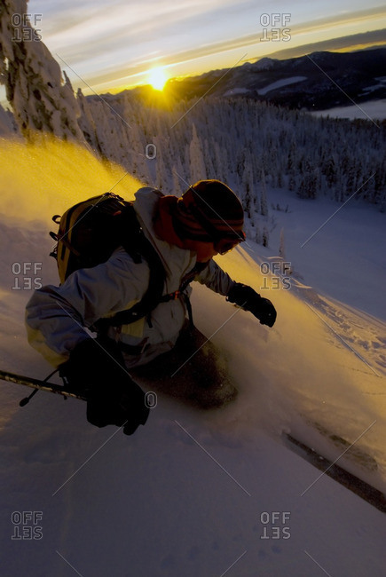Woman Whitewater backcountry skiing in powder with sunset and alpenglow on snow, descent of Evening Ridge, Nelson, British Columbia, Canada.