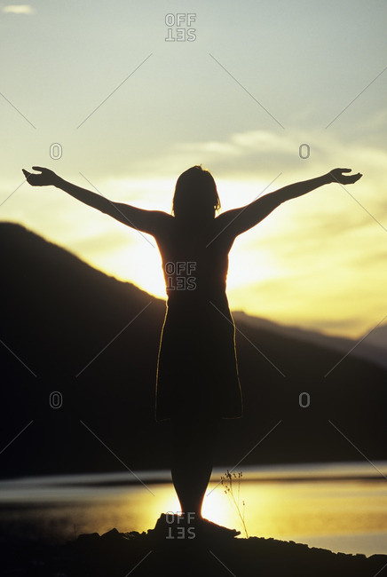 Woman with arms raise at sunset, Columbia River, Revelstoke, British Columbia, Canada.