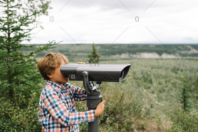 Boy looking through a viewing scope on the edge of a forest
