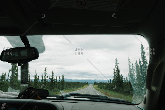 An empty road in the Alaskan wilderness visible through the windshield of a car