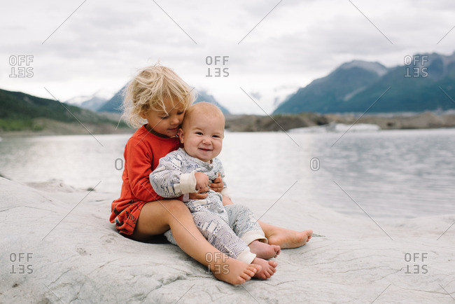 Two children sitting together on a rocky outcropping overlooking a lake