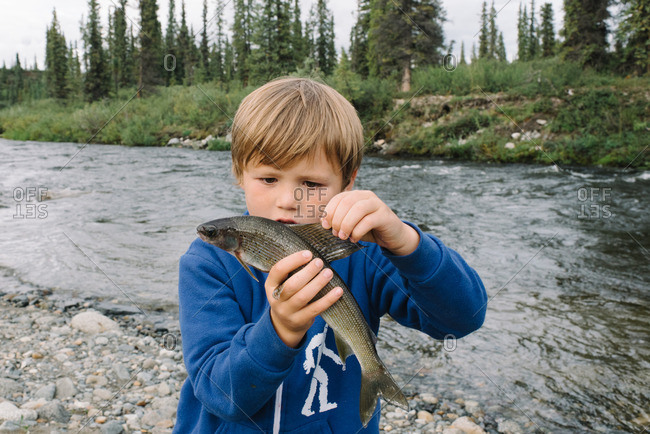 Boy holding a fish along a rocky riverside