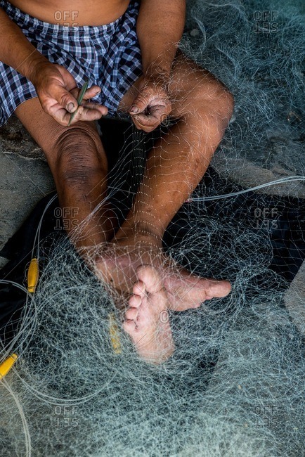 Vietnamese man stitching a fishing net