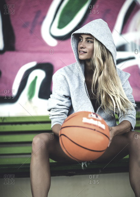 Woman sitting on a bench wearing a hooded sweatshirt and holding a basketball