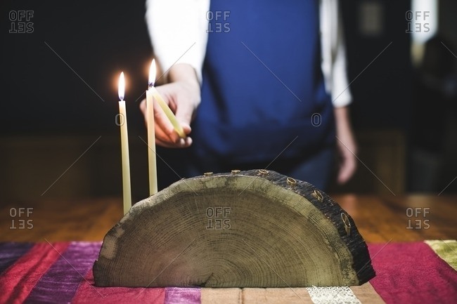 Woman lighting a third candle on a menorah made from a log