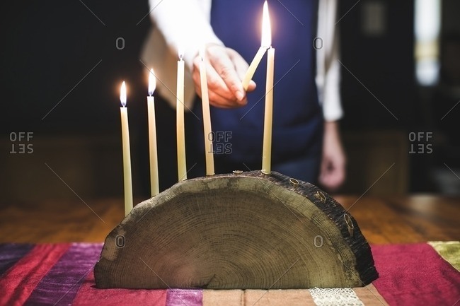 Woman lighting a sixth candle on a menorah made from a log
