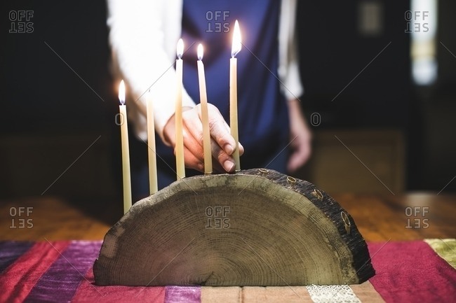 Woman placing a fifth lit candle on a menorah made from a log