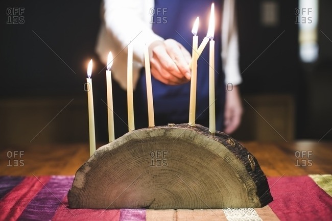 Woman lighting a seventh candle on a menorah made from a log