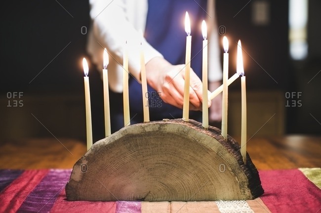 Woman lighting a ninth and final candle on a menorah made from a log